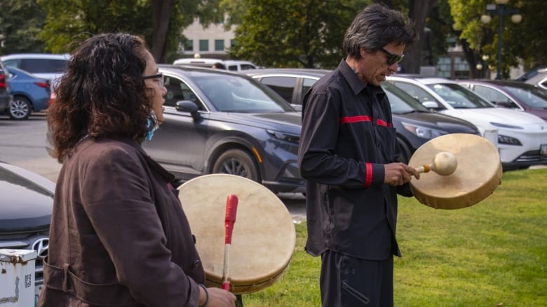 Two people hold hand drums and sing