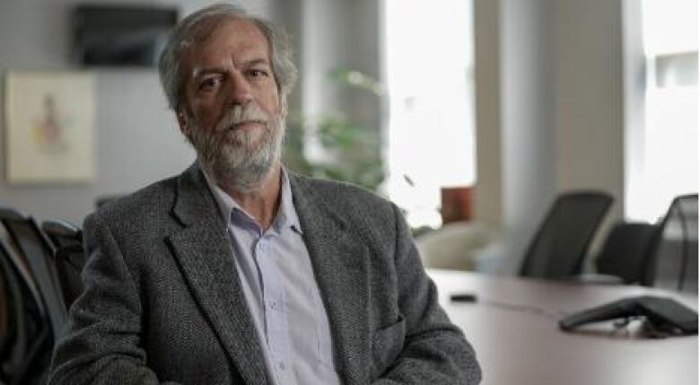 A bearded man in a suit sits in an office