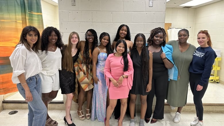 11 women, of them 6 are students at Weston Collegiate Institute, standing in front of a fitting room at the high school where the girls tried on dresses ahead of the gala. 