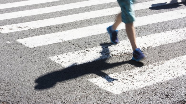 A boy's legs seen walking across a crosswalk on a road.