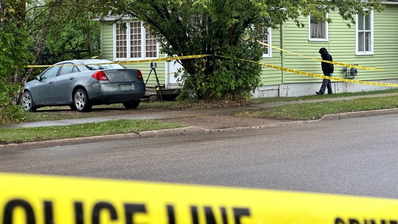 A small green bungalow surrounded by yellow police tape. 