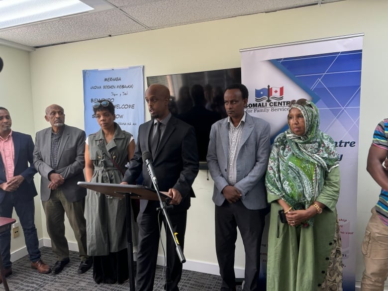 Several members of the Somali community standing hosting a press conference in a room. 