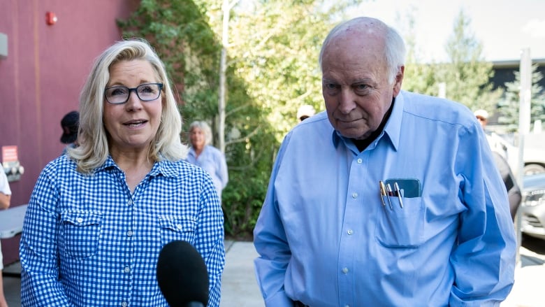 Liz Cheney and Dick Cheney speak to members of the media in front of a library as people with cameras and phones look on. 