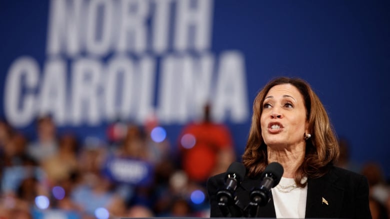 Harris speaking in front of sign that says 