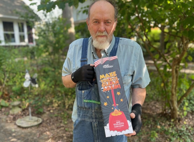 Older man in denim overalls shows off toilet brush that looks like Trump