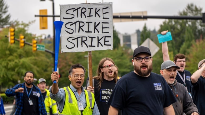 A group of men walk on a street, one carries a sign saying, 'Strike, strike, strike.'