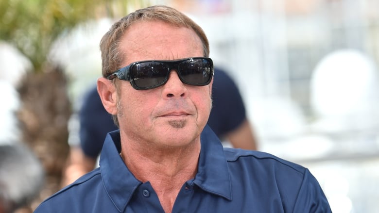 A middle-aged, cleanshaven man is shown wearing sunglasses and a polo shirt in a closeup.