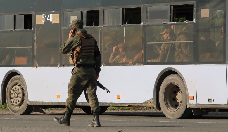 A soldier talks on a phone as he walks on a road near a bus carrying other soldiers.