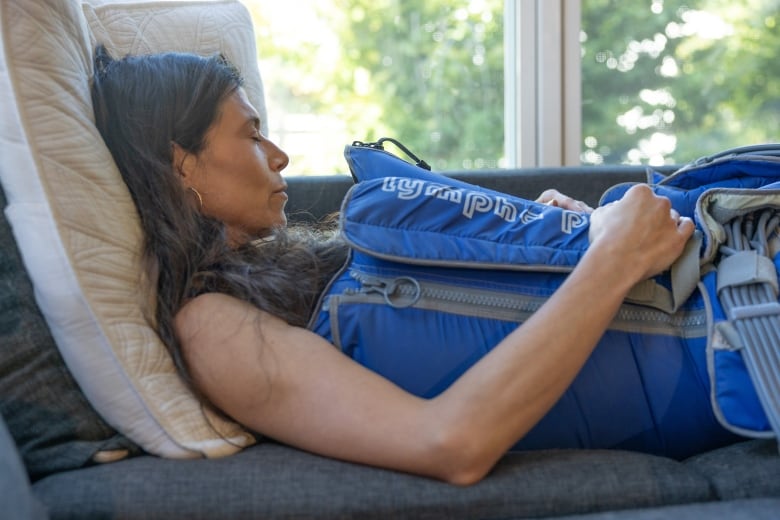 A woman is lying on a couch with her eyes closed. She is wearing a blue inflatable suit that is zipped up on the side.