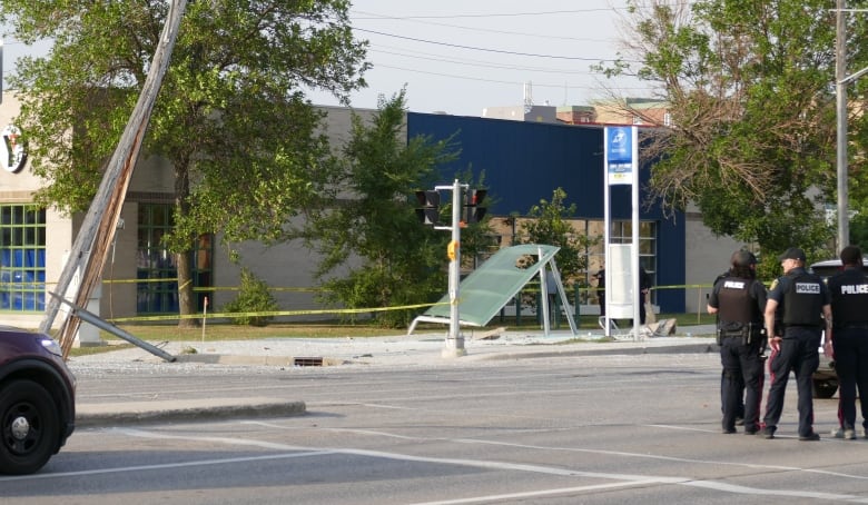 A damaged bus shelter can be seen in the background with a group of police officers to the right of the photo.