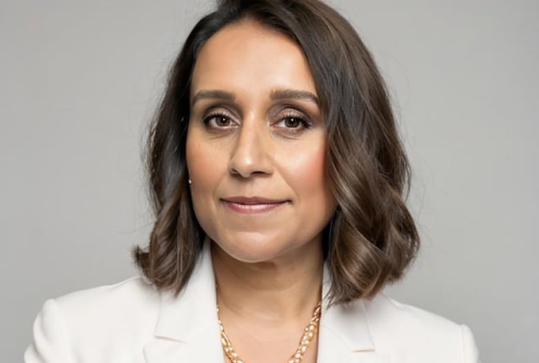 Woman with brown hair wearing a white blazer and golden necklace. 