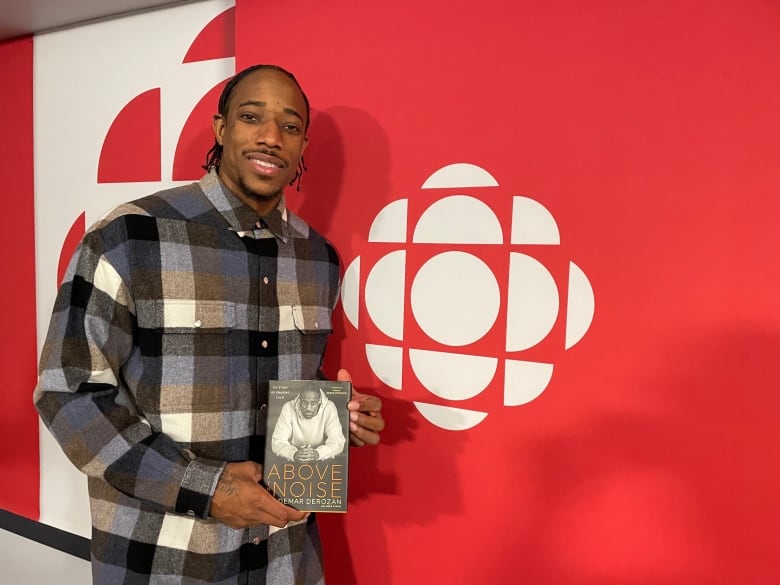 A man holds a book in front of a CBC logo.