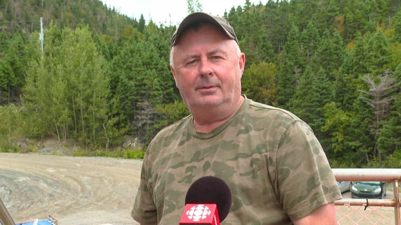 A man wearing a green ballcap and camoflauge tshirt looks directly into. the camera