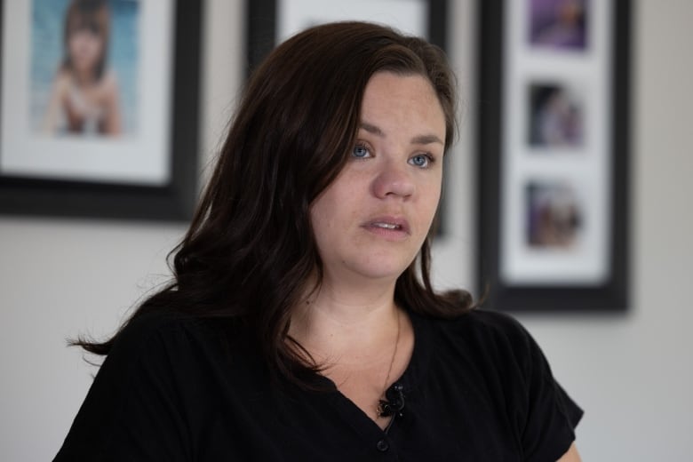 A Caucasian woman with brown shoulder length hair and blue eyes stands in front of a wall of family photos.