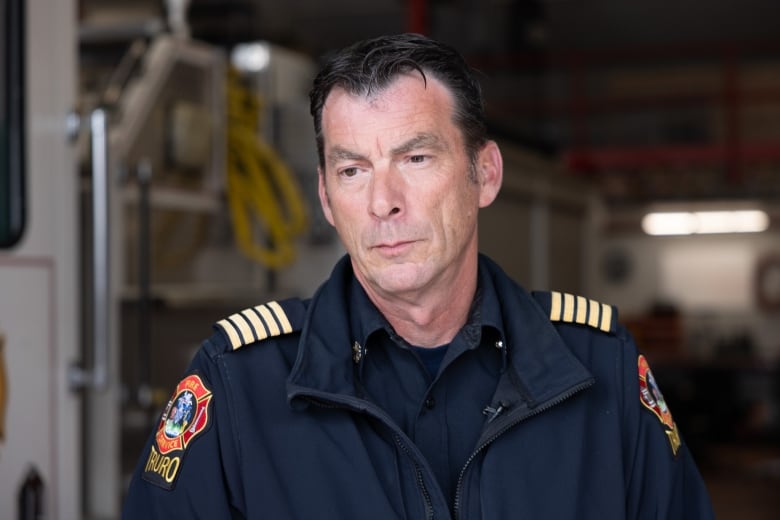 A man wearing a firefighters uniform stands in front of a white fire truck.