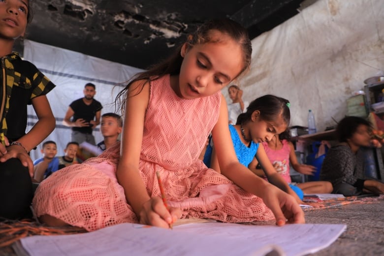 a little girl in a pink dress writes notes in a notebook