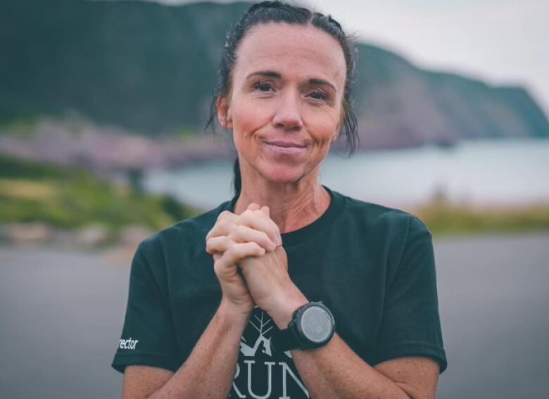 A woman in a green t-shirt clasps her hands in front of her chest. She has a slight smile.