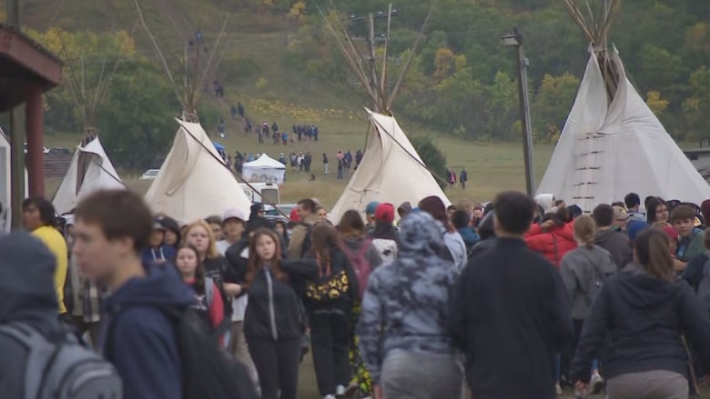 people are walking outside, there are teepees in the background