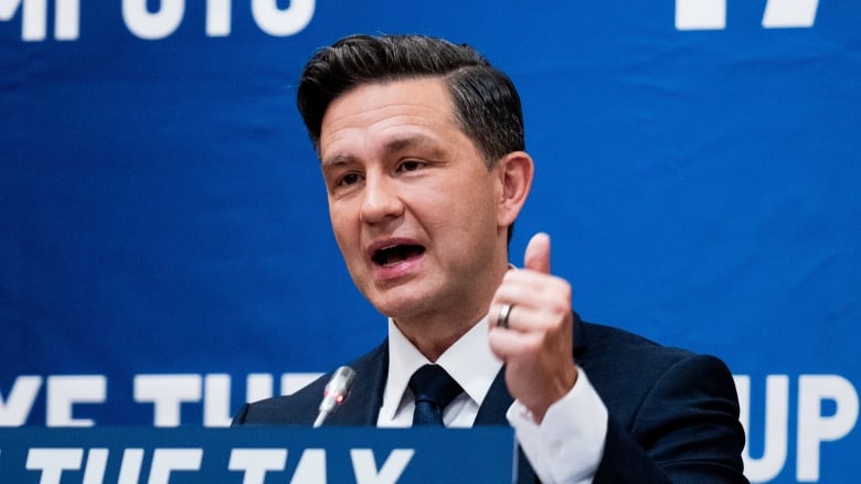 A man in a suit gestures with his left hand as he speakts at a podium.