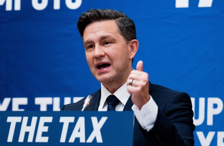 A man in a suit gestures with his left hand as he speakts at a podium.