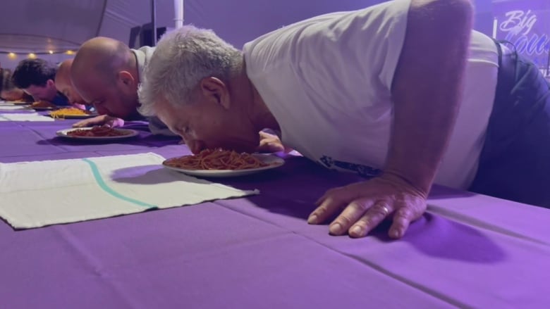 People are crouched over a table, with their mouths on a plate of pasta. 