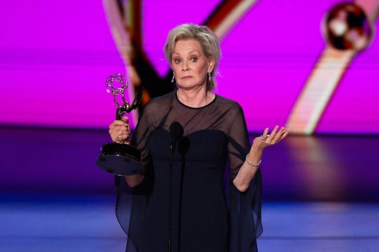 A person holding an award gestures while speaking onstage.