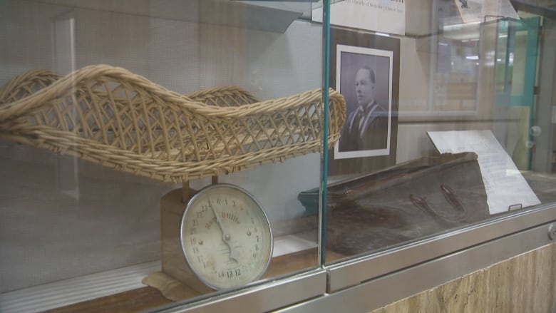 Weighing scales and a black and white photo are shown in a glass case.