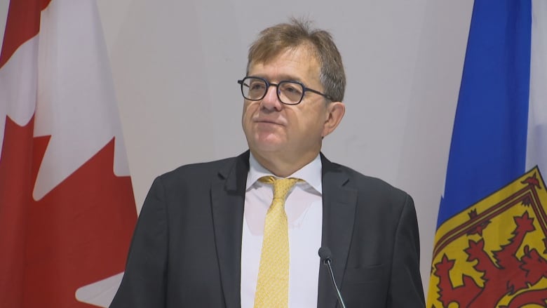 Man in suit and glasses stands behind a podium.