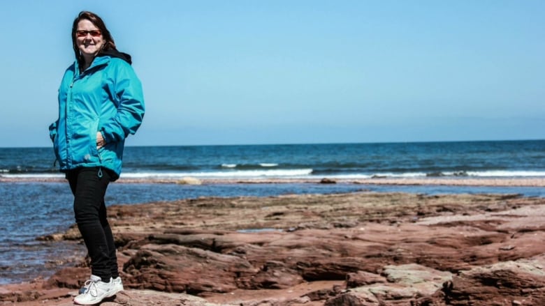 Woman in blue jacket standing on rocks by the sea.