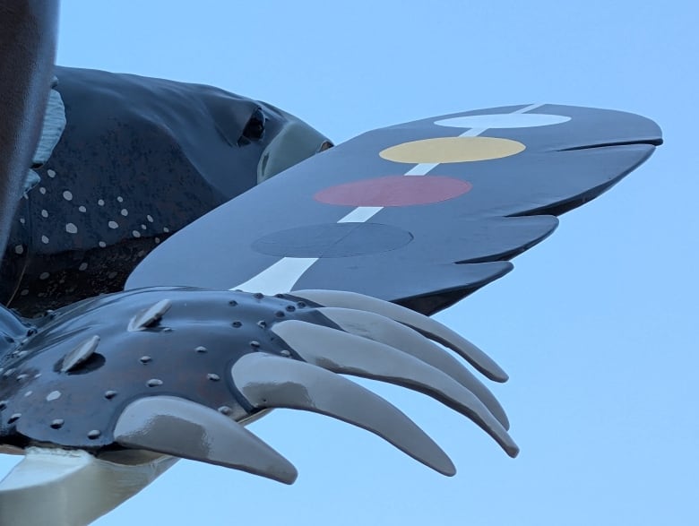 A close-up of the feather in the turtle's hand with black, red, yellow and white dots down the spine of it.