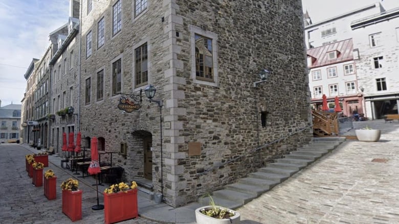 A stone building on a cobblestone street with patio tables set up outside.