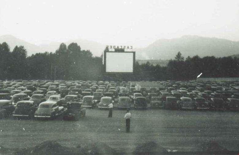 A black-and-white picture of a series of cars lined up at a drive-in theatre.