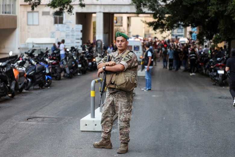 A soldier in uniform, including a green beret, stands with a gun near a hospital.