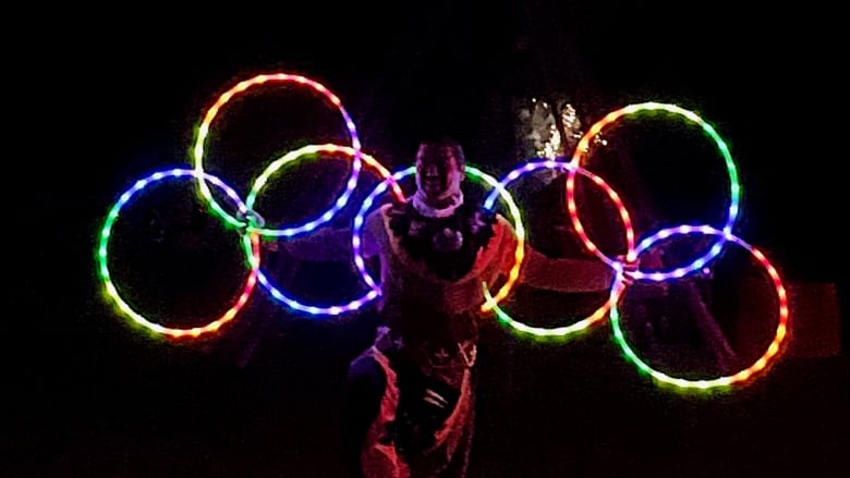 A person stands in total darkness holding several glowing hoops.