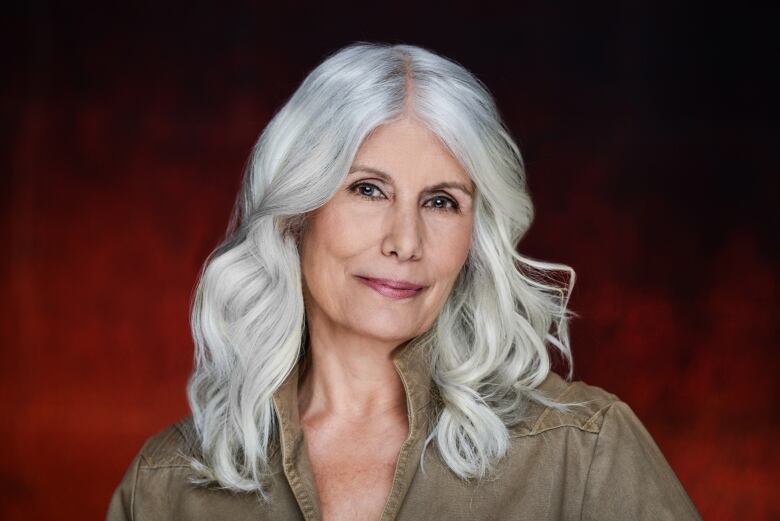 Indigenous woman with grey hair looks confidently at camera. Red background.