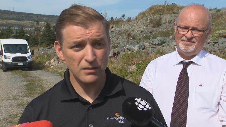 A man wearing a black polo shirt stands in an off-road area.