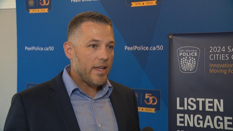 John Versluis, the Manager of Community Safety and Well-Being at Peel Regional Police, standing in front of a blue backdrop as he speaks 