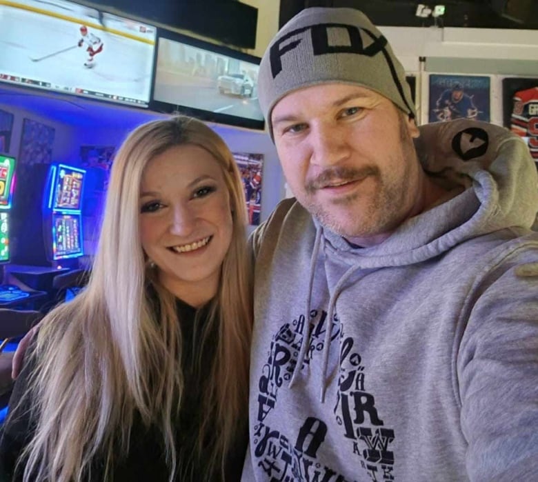 A man and woman smile for a selfie with gaming machines in the background. 