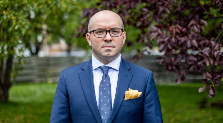 A person wearing a blue suit stands outside.