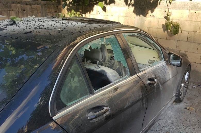 A black sedan is seen with shattered windows after an explosion.