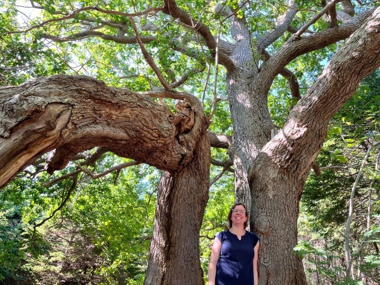 A woman standing near a tall oak tree. 