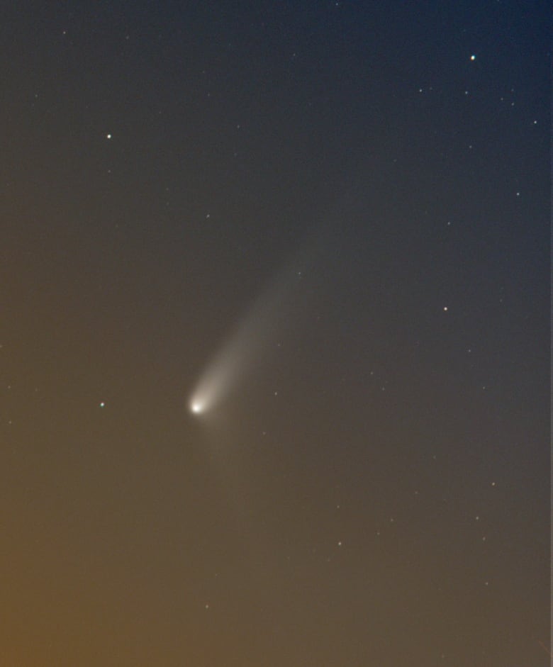 A bright object with a tail is seen in the early morning sky.