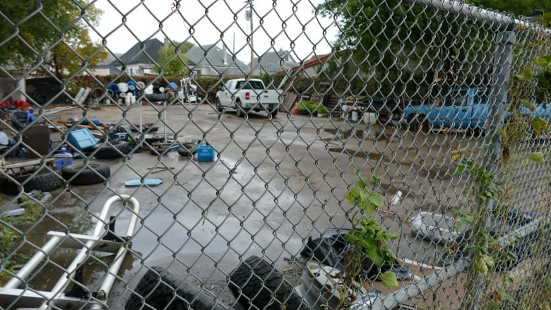 A white pickup truck, a blue pickup and a jumble of tires and other detritus are seen in a fenced-off lot.