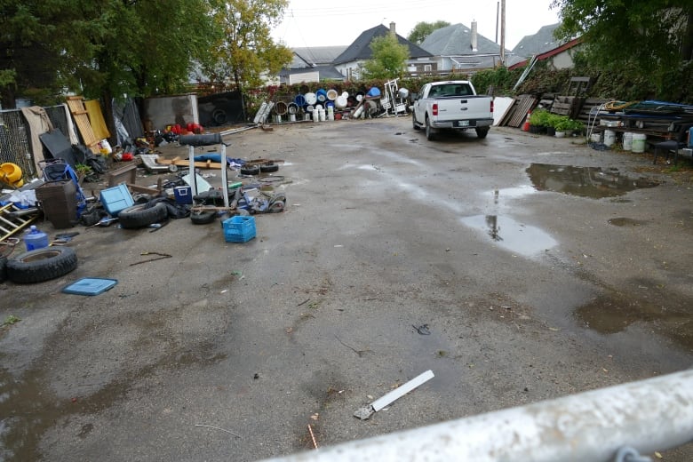 A white pickup truck sits in a lot with a variety of items piled along the fences.