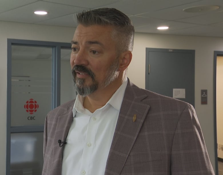 A man wearing a suit stands in the CBC newsroom.