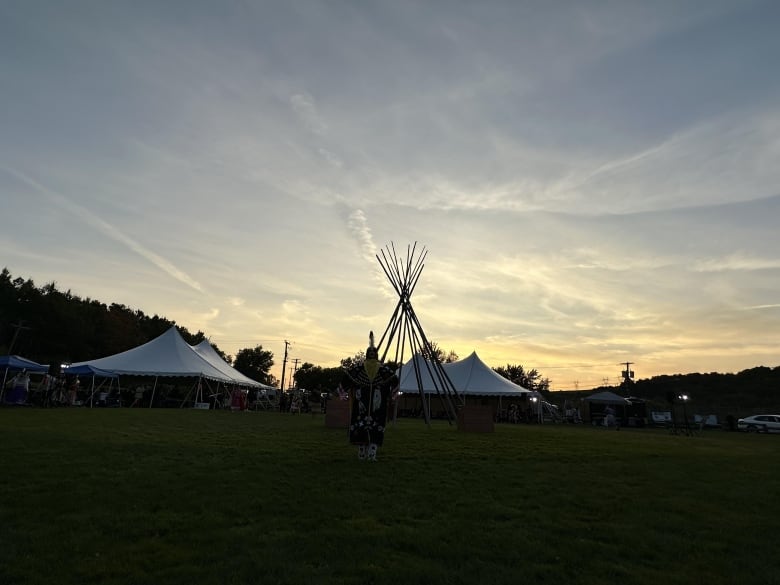 White tents and a teepee are set up on a grassy lawn as the sun rises.