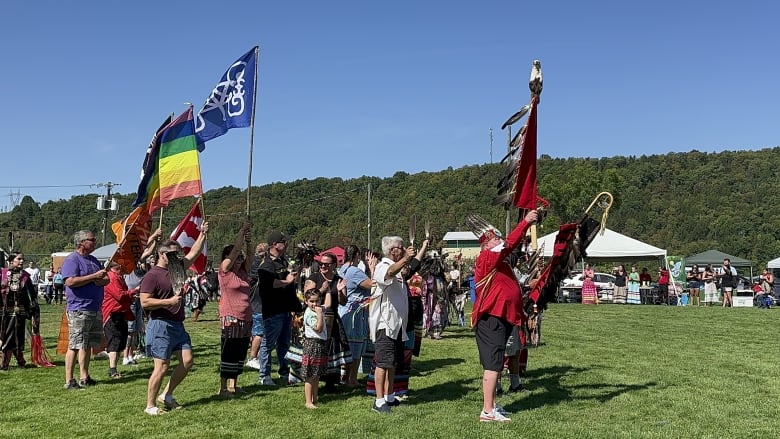 A group of people stand on a grassy lawn, some holding flags.