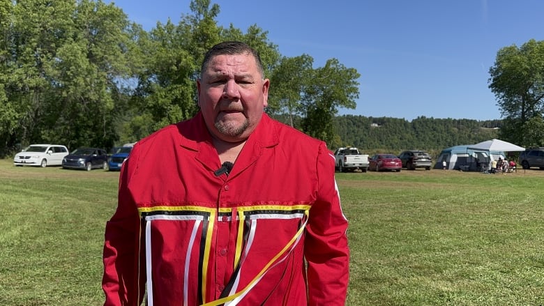 A man dressed in a bright red shirt with yellow, black and white lines stands on a grassy lawn.