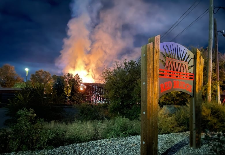 A sign for the Red Bridge in the foreground right, with the structure in flames in the distance.