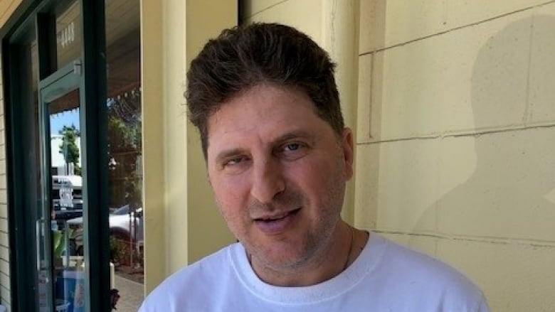 A middle-aged man with short brown hair and a white T-shirt smiles slightly at the camera. 